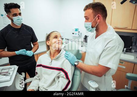 Caucasian smiling female lying on doctors bed while chatting to male nurses in doctors office Stock Photo