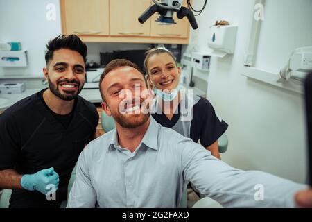 Caucasian male taking selfie with male and female nurse wearing surgical masks in doctors office Stock Photo