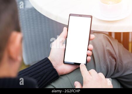 Close up of man's hands holding mobile smart phone with blank copy space screen. Image of man sitting at a table with a coffee in cafe and using mobil Stock Photo