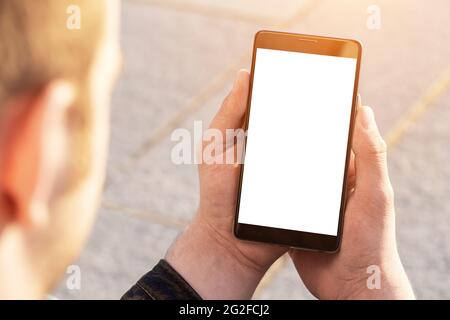 Man uses his Mobile Phone outdoor, close up. Mockup image blank white screen cell phone. Men hand holding texting using mobile phone outdoor. Stock Photo