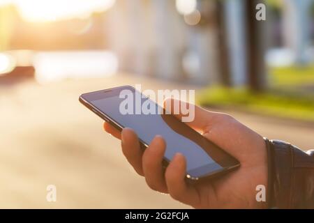 Man uses his Mobile Phone outdoor, close up. Men hand holding texting using mobile phone outdoor. Stock Photo