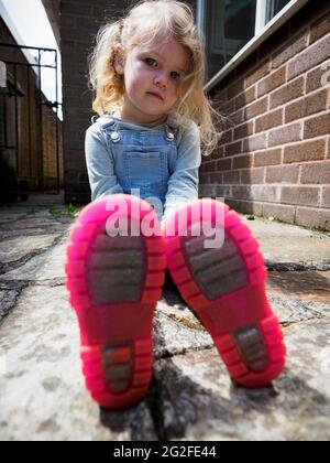 Young child sat on the floor outside, Devon, UK Stock Photo