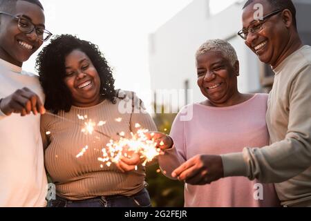 Happy African family celebrating with sparklers fireworks at house party - Parents unity and holidays concept Stock Photo