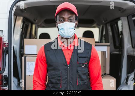 African delivery man working while wearing face mask to avoid corona virus spread - People working with fast deliver during corona virus outbreak Stock Photo
