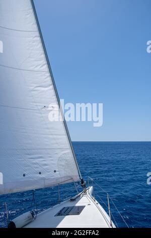 White sloop rigged yacht sailing in open calm ocean, blue sky background, sunny day. Sailboat deck, bow, mast and sails closeup view. Leisure activity Stock Photo