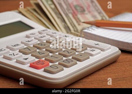 close-up of calculator with notepad, pencil and dollar bills in background Stock Photo