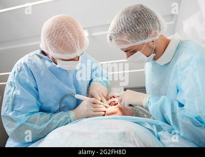 Close-up dental surgery process. Implantation. Dentist surgeon with assistant, wearing disposable clothes, during work using modern technology. Stomatology and health care concept. Stock Photo