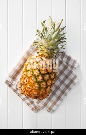 Whole pineapple on checkered napkin on white table. Top view. Stock Photo