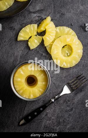 Canned sliced pineapple fruit on black table. Top view. Stock Photo