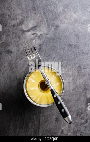 Canned sliced pineapple fruit in can with fork on black table. Top view. Stock Photo