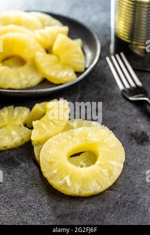 Canned sliced pineapple fruit on black table. Stock Photo