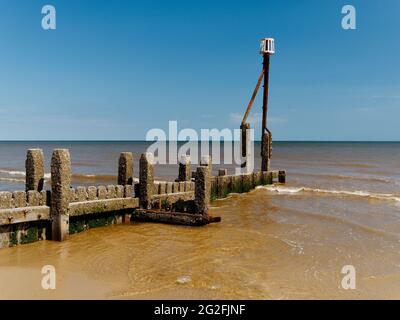 Barnacle encrusted groynes rise from the yellow sands of Mundesley beach, a small North Noroflk seaside resort. Stock Photo