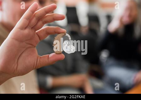 A young man puts on a hearing aid. Portable sound amplifier for the deaf and hearing impaired Stock Photo