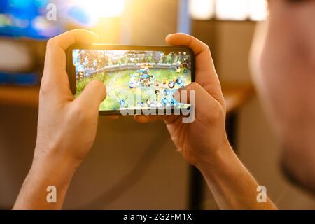 Caucasian guy playing video game on his mobile phone at home Stock Photo