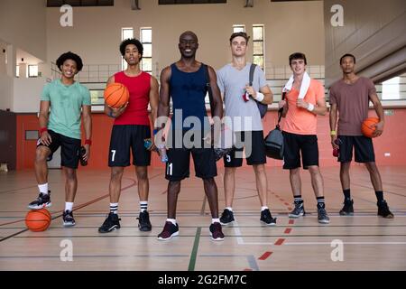 Portrait of diverse male basketball team and coach smiling and holding balls Stock Photo