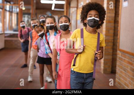 Portrait of group of diverse students wearing face masks while standing in the corridor at school Stock Photo
