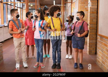 Group of diverse students wearing face masks talking to each other in the corridor at school Stock Photo