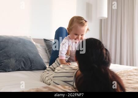 Portrait of caucasian mother playing with her baby lying on the bed at home Stock Photo