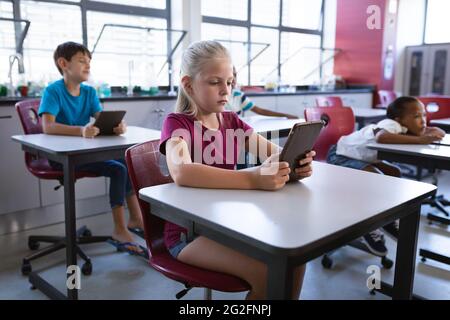 Caucasian girl using digital tablet while sitting on her desk in the class at school Stock Photo