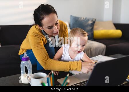 Caucasian mother holding her baby using laptop while working from home Stock Photo