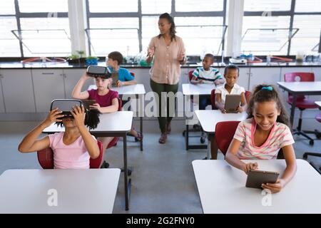 African american female teacher teaching students to use electronic devices in the class at school Stock Photo