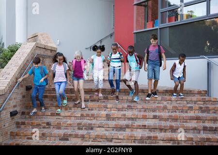 Group of diverse students with backpacks walking down the stairs together at school Stock Photo