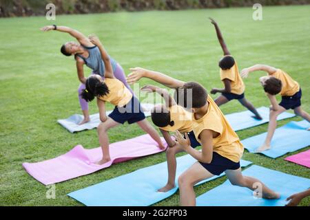 Female teacher and group of diverse students performing stretching exercise in the garden at school Stock Photo
