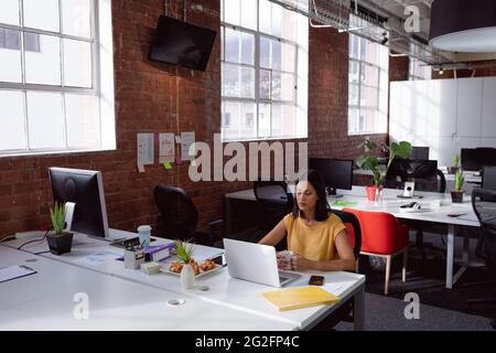 Thoughtful caucasian businesswoman sitting at desk in office using laptop and holding coffee cup Stock Photo