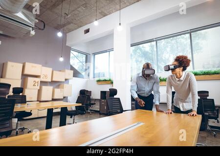 Two diverse businesspeople sitting at table and using vr headsets Stock Photo