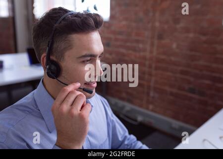 Caucasian businessman wearing phone headset sitting at desk using computer Stock Photo