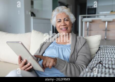 Portrait of mixed race senior woman sitting on sofa using tablet Stock Photo