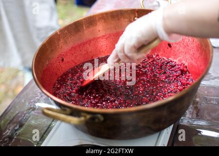 Cooking Finnish lingonberry jam with spices in a copper basin on a gas stove. Female hand with spoon Stock Photo