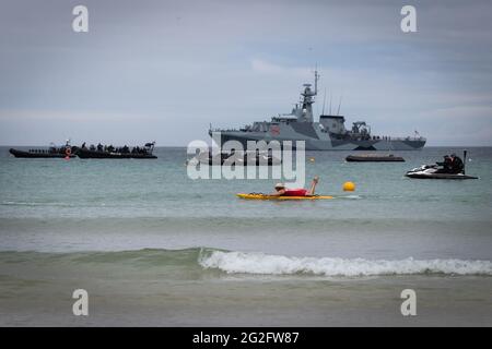 St Ives, UK. 11th June, 2021. A paddle boarder swims past the Royal Navy which has been deployed for the G7 Summit. Credit: Andy Barton/Alamy Live News Stock Photo