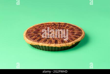 Homemade pecan cake isolated on a green background. Whole pie with pecan nuts in its tray on a colored table Stock Photo