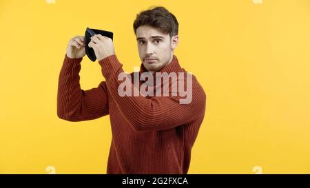 Upset man holding empty wallet isolated on yellow Stock Photo