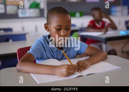 African american boy studying while sitting on his desk in the class at ...