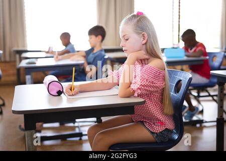 Caucasian girl studying while sitting on her desk in the class at school Stock Photo