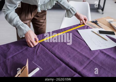 Cropped view of seamstress measuring cloth near cellphone and sketches Stock Photo