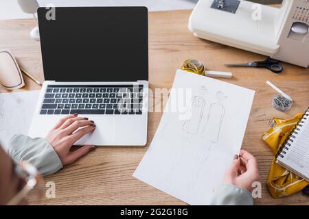 Blurred designer using laptop and holding sketches in atelier Stock Photo