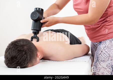 Massage gun background. Young female physiotherapist using handheld massaging gun to relieve neck muscle pain during physical therapy session.