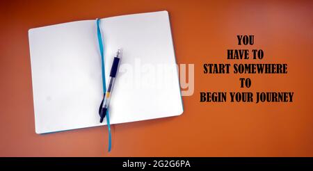 Selective focus on the note book and a pen.  A text quoting You have to start sonwhere to begin your journey. Stock Photo
