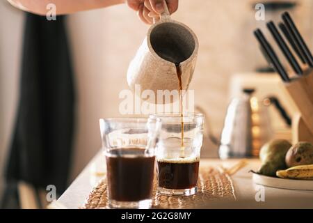 Pouring black coffee from ceramic pot into the glasses in the ho Stock Photo