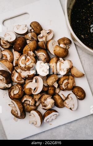 Sliced Baby Bella Mushrooms on a white cutting board Stock Photo