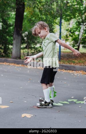 5 years old boy kid playing outdoors, children outdoor activities, wearing green t-shirt with dinosaurus print and dino helmet Stock Photo