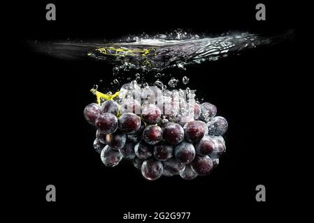 Isolated Red grapes splashing and sinking in water on black Stock Photo