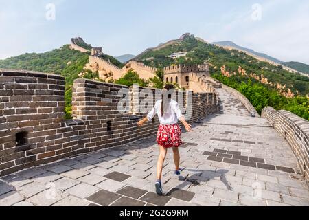 Happy cheerful joyful tourist woman at Great Wall of china having fun on travel smiling laughing and dancing during vacation trip in Asia. Girl Stock Photo