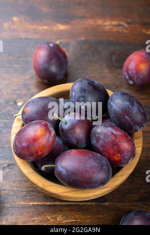 Fresh plums in a wooden bowl on a brown table. Gathering the summer harvest. Stock Photo