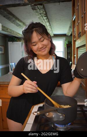 US Asian Woman cooking in kitchen, smiling at food Stock Photo