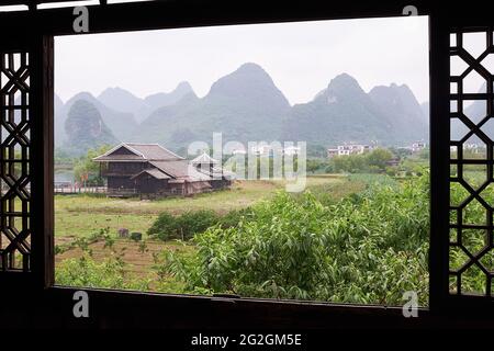 Window framed view of the lush green farmland, buildings and majestic karst mountains landscape of Shangri-la Park, Guilin, China Stock Photo