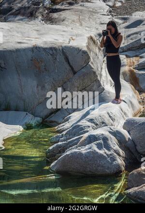 Impressions from Lavertezzo in the Verzasca Valley, Locarno district, Canton Ticino in Switzerland: popular excursion destination for hiking, river diving and swimming. Young woman taking photos. Stock Photo